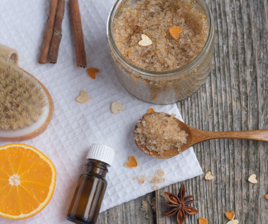 Jar of sugar scrub, spoon, amber bottle and slice of orange on a white cloth